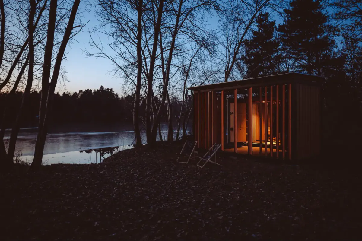 Osvětlená Sauna Pardubice ve Stéblové u jezera za soumraku.